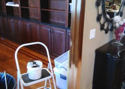 A step ladder with a brush laying on a bucket of stain next to a door frame being stained
