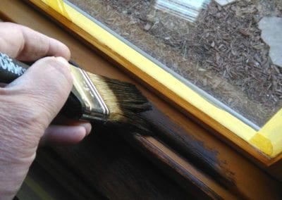 A hand holding a brush staining a window frame